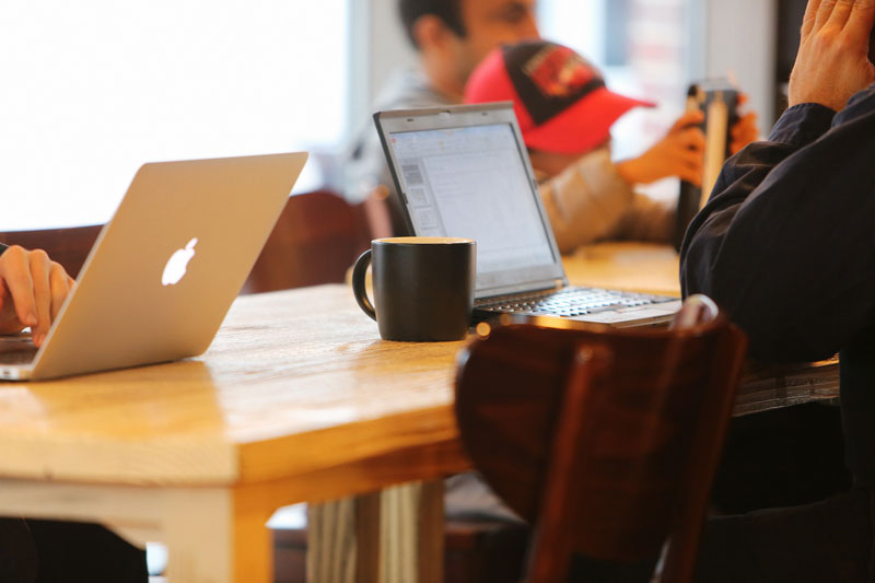 3 laptop users in a coffee shop at a wooden table